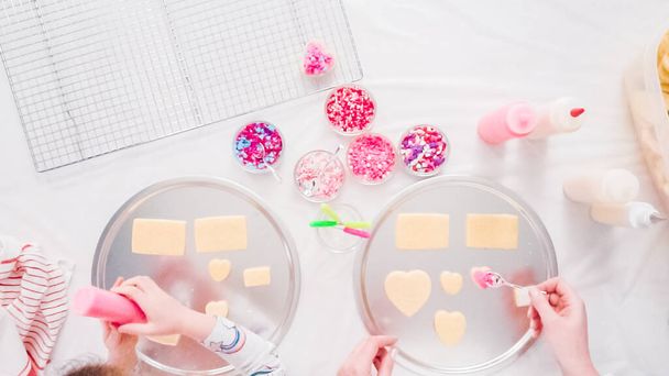 Flat lay. Step by step. Little girl decarting sugar cookies with royal icing and sprinkles for Valentine's Day. - Foto, Imagem