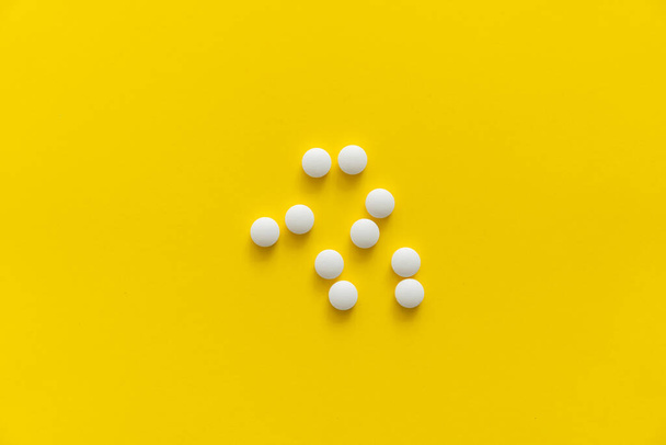 White pills on yellow background. Medicine, medication, painkillers, tablet, medicaments, drugs, antibiotic, vitamin, treatment. Pharmacy theme. Top view on the pills scattered on the white surface. - Фото, изображение