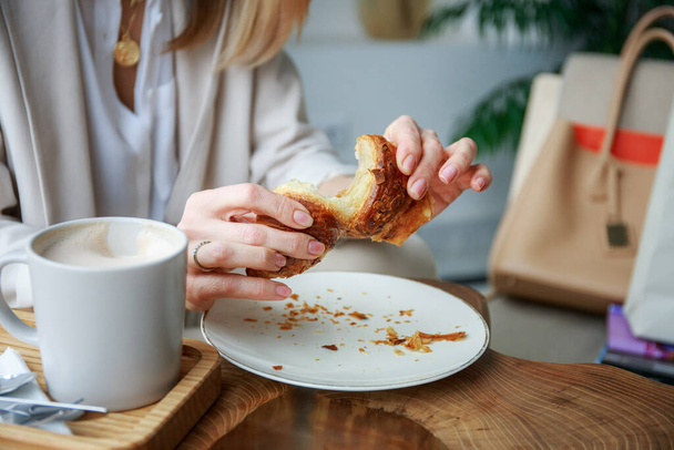 The girl breaks a croissant with her hands - Photo, Image