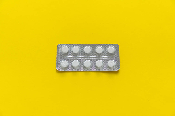 Top view on the pills in the package. White pills on yellow background. Medicine, medication, painkillers, tablet, medicaments, drugs, antibiotic, vitamin, treatment, capsule, dose. Pharmacy theme. - Foto, immagini