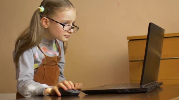 Linda niña en eyeglassess está sentada frente a su portátil negro y estudiar en casa debido a la pandemia de Coronavirus Covid-19 y auto-aislamiento. Concepto de educación remota
 - Metraje, vídeo