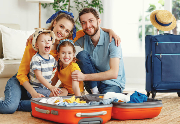 Happy parents with children laughing at camera while sitting on floor near sofa with suitcases near at hom - Photo, Image