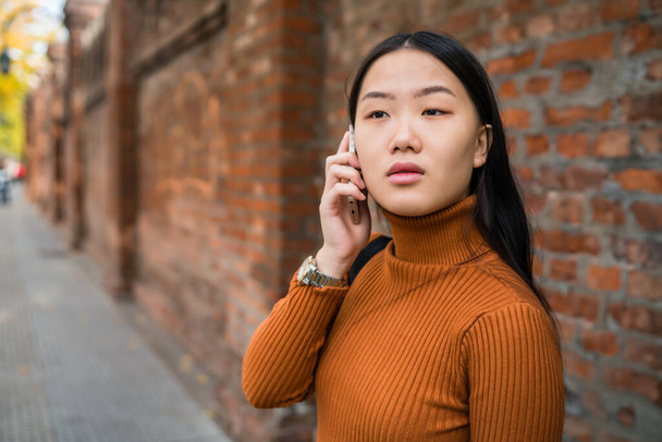 Portrait of young Asian woman talking on the phone outdoors in the street. Urban and communication concept. - Foto, imagen