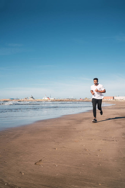 Portrait of an athletic man running at the beach. Sport, fitness and healthy lifestyle. - Photo, image