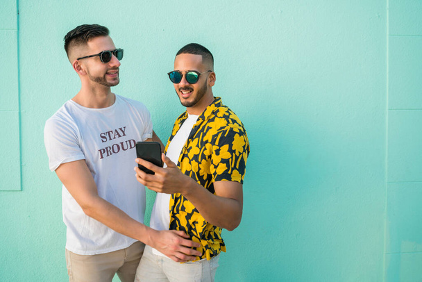 Portrait of happy gay couple spending time together while using mobile phone. Lgbt and love concept. - Zdjęcie, obraz