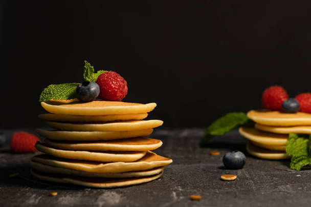Großaufnahme eines Stapels Pfannkuchen mit Beeren (Blaubeeren, Himbeeren) und Minze auf dunklem Hintergrund. - Foto, Bild