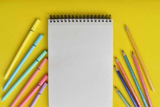 Libreta blanca con lapices y marcadores de colores sobre fondo amarillo - Φωτογραφία, εικόνα