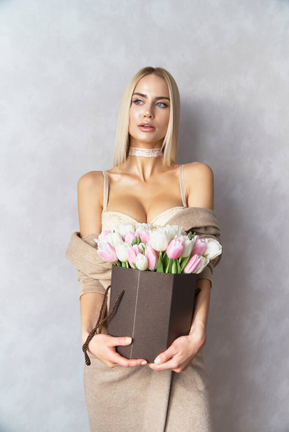 Beautiful sexy blonde woman blue eyes in sexy beige lingerie with spring flowers bouquet light pink and white colored formed in gift box for you any celebrating - Foto, Bild