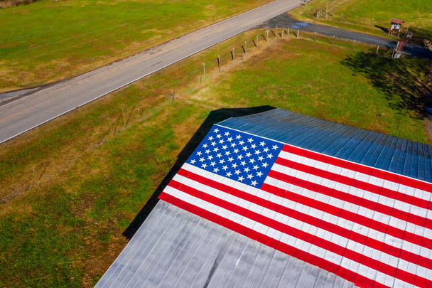 Een landweg met een Amerikaanse vlag geschilderd op een schuur nabij een boerderij in de Verenigde Staten - Foto, afbeelding