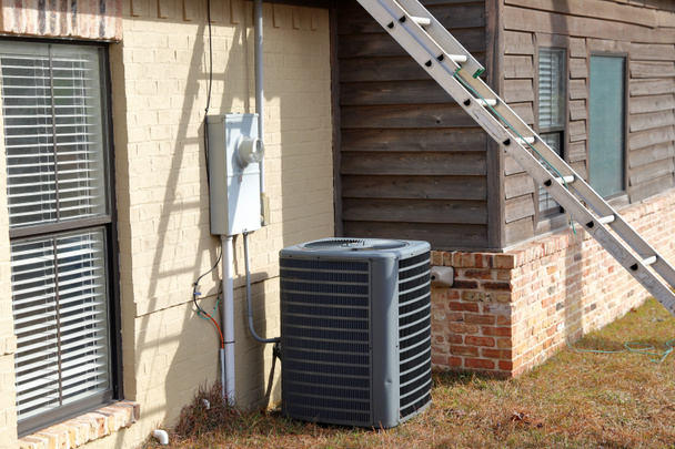 Graue Klimaanlage Kondensatorkompressoranlage neben gemäldetem Backsteinhaus mit Leiter gegen Haus - Foto, Bild