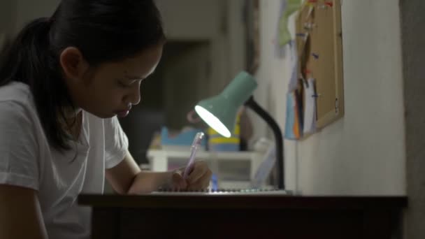 Ασιάτης χαριτωμένο κορίτσι μελέτη και το γράψιμο κατά τη διάρκεια της εργασίας στο γραφείο το βράδυ. Εκπαίδευση και σοφία. - Πλάνα, βίντεο