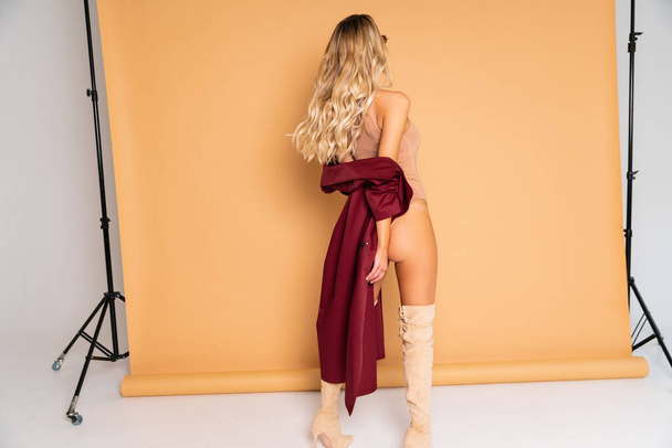 Sexy Blonde model with perfect skinny body with huge boobs posing in beige combidress and glam red coat so good fashion style retouched in very high quality - 写真・画像