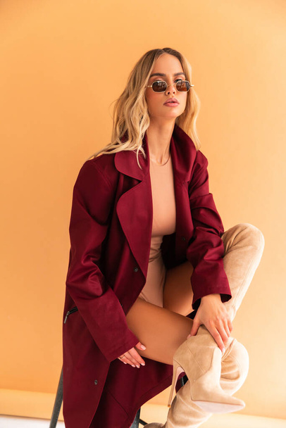 Sexy Blonde model with perfect skinny body with huge boobs posing in beige combidress and glam red coat so good fashion style retouched in very high quality - Photo, image