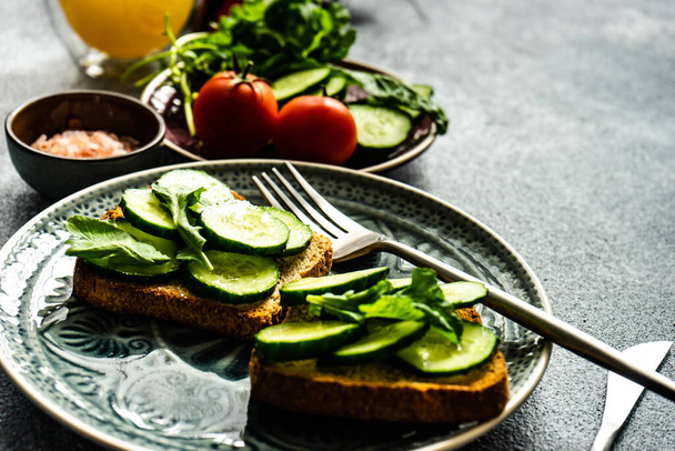 Gezond lunchconcept met toastjes met biologische komkommer, raketkruid en roze zout op stenen achtergrond met kopieerruimte - Foto, afbeelding