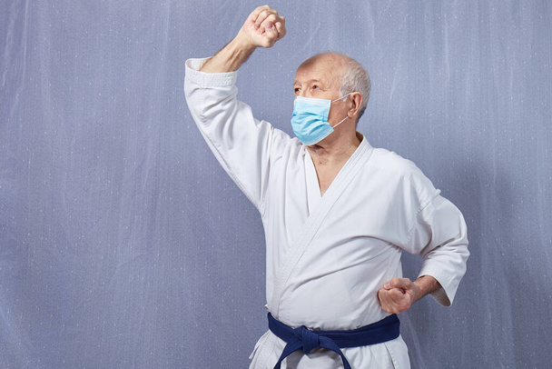 Velho atleta masculino em uma máscara médica executa blocos com as mãos
 - Foto, Imagem
