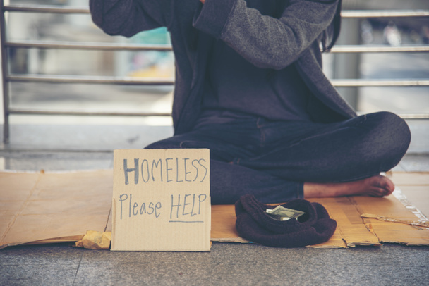 ホームレスの人々の貧困乞食の男性はお金の仕事を求めて、無力な汚れた都市の段ボール箱の兆候に座って助けを願っている"ホームレスを助けてください"ボード上の。都市のコンセプトで乞食. - 写真・画像