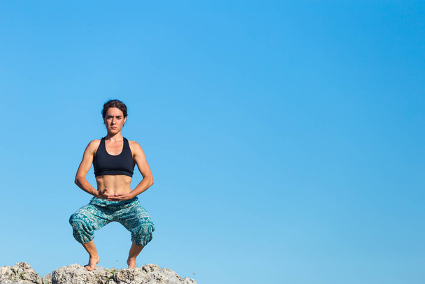 Fille pratique le yoga au sommet de la montagne, femme effectue asanas debout sur une grande pierre sur un fond de montagnes et un ciel, Méditation dans la nature, Exercice pour le développement de l'équilibre. - Photo, image