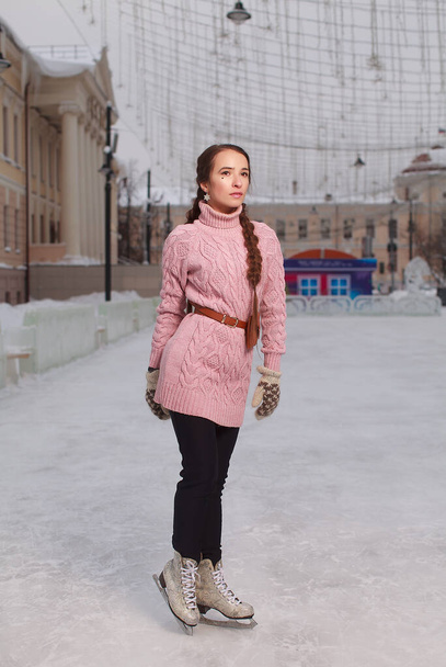 Young pretty woman dressed pink sweatshirt standing on ice in skates, outdoor ice-scating rink - Zdjęcie, obraz