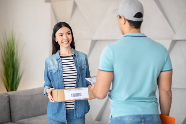 Dark-haired female holding parcel, brunette male courier standing in front of her - Foto, Imagen