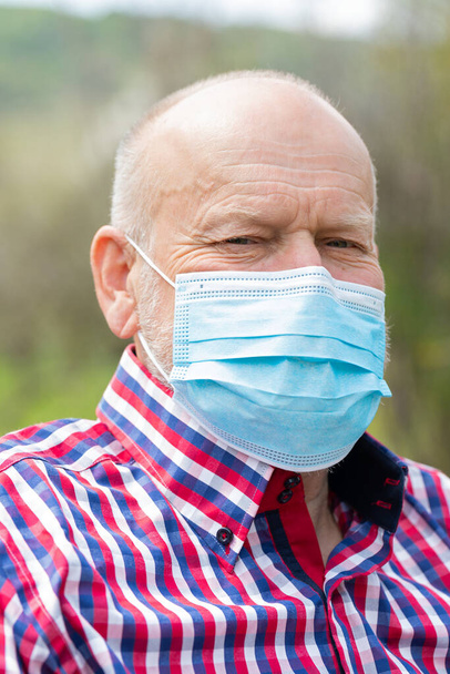 Portrait of elderly man with surgical mask spending time outdoors in the garden  - Photo, image