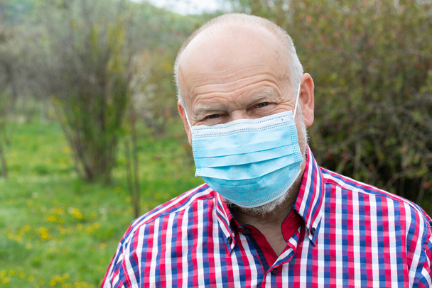 Portrait of elderly man with surgical mask spending time outdoors in the garden  - 写真・画像