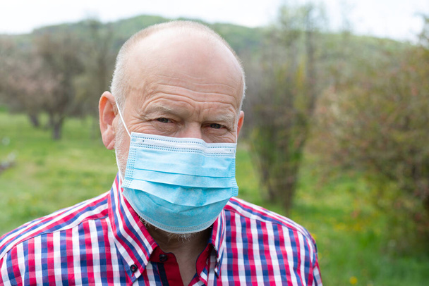 Portrait of elderly man with surgical mask spending time outdoors in the garden  - 写真・画像