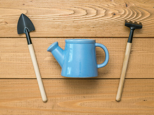 Голубая банка для полива между лопатой и грабли на деревянном фоне
. - Фото, изображение