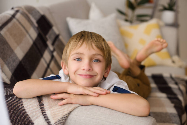 portret van mooie kleine jongen liggend op zijn buik op de bank, met geblokte ruitjes, in kamer thuis - Foto, afbeelding