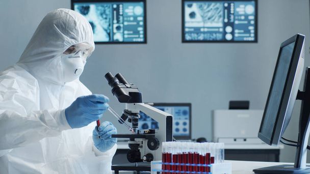 Scientist in protection suit and masks working in research lab using laboratory equipment: microscopes, test tubes. Coronavirus 2019-ncov hazard, pharmaceutical discovery, bacteriology and virology - Zdjęcie, obraz