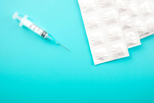 Embalagens de seringa médica e comprimidos brancos sobre fundo azul
.  - Foto, Imagem