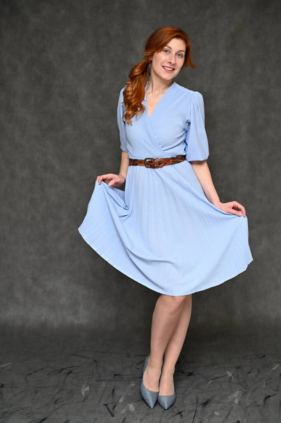 Full-length Vertical Portrait of a young pretty red-haired woman in a blue dress on a gray background. Model demonstrates standing different poses. - Foto, Imagem