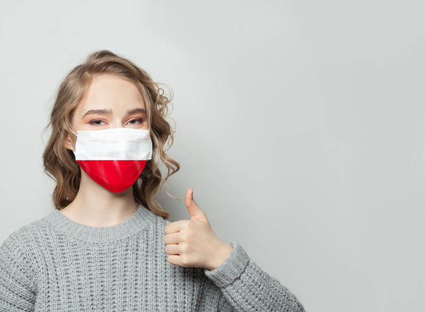 Szczęśliwa kobieta w masce trzymająca kciuk w górze z tłem flagi Polski. Koncepcja epidemii grypy i ochrony przed wirusami - Zdjęcie, obraz