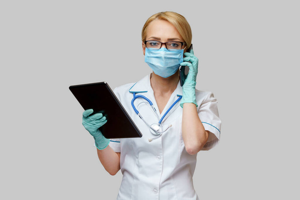medical doctor nurse woman wearing protective mask and gloves - holding tablet pc and mobile phone - Foto, imagen