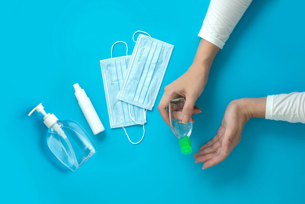 Vrouwen handen houden hand sanitizer met alcohol spray en chirurgische masker op blauwe achtergrond - Foto, afbeelding