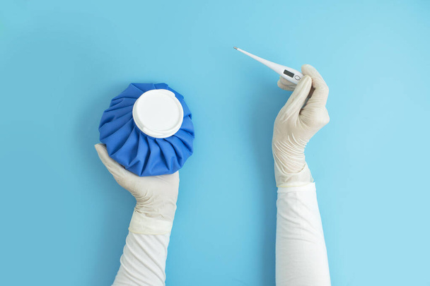 Naisten kädet yllään kirurginen käsine tilalla korva lämpömittari ja jääpussi mittaus lämpötila sinisellä pohjalla
 - Valokuva, kuva