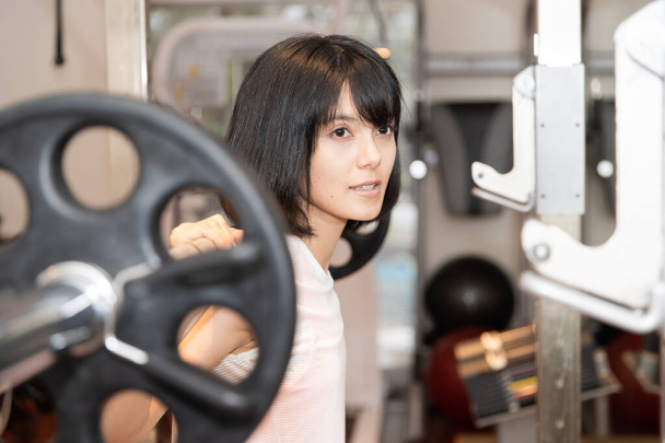 Ασιάτισσα γυναίκα κάνει μυϊκή εκπαίδευση με τον εξοπλισμό στο προσωπικό γυμναστήριο - Φωτογραφία, εικόνα