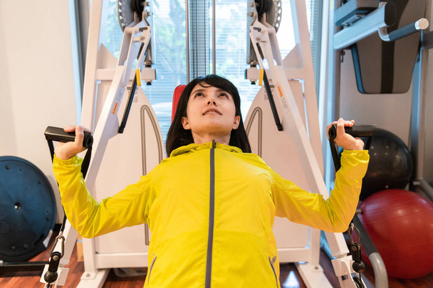 Mujer asiática haciendo entrenamiento muscular con equipo en gimnasio personal
 - Foto, Imagen