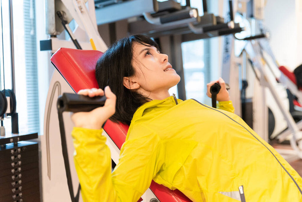 Mujer asiática haciendo entrenamiento muscular con equipo en gimnasio personal
 - Foto, imagen