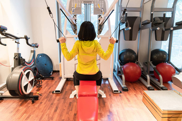 Азиатка, занимающаяся тренировкой мышц с оборудованием в личном спортзале
 - Фото, изображение