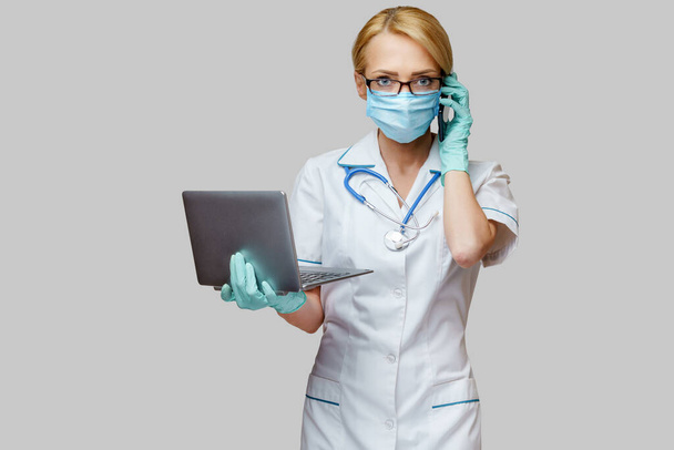 orvos nővér nő visel védő maszk és kesztyű - gazdaság laptop és mobil telefon - Fotó, kép