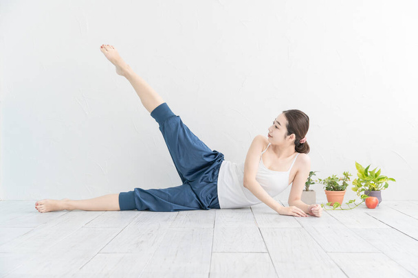 Asiática joven mujer haciendo suave ejercicio en un brillante habitación
 - Foto, Imagen