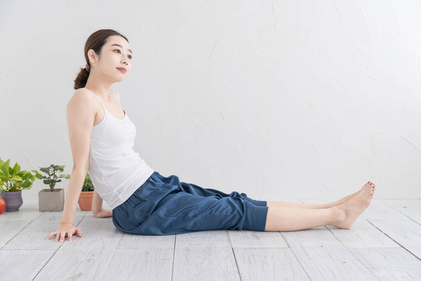 Asiática joven mujer haciendo suave ejercicio en un brillante habitación
 - Foto, Imagen