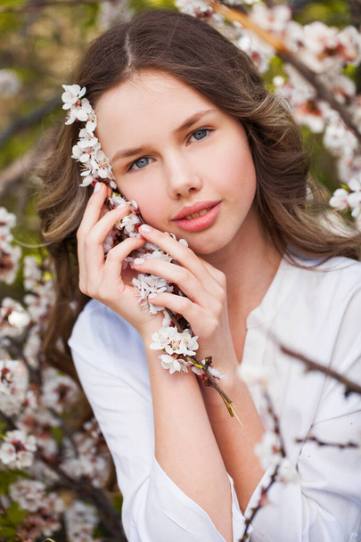 Pretty teen girl are posing in garden near blossom cherry tree with white flowers. Spring time  - Fotografie, Obrázek