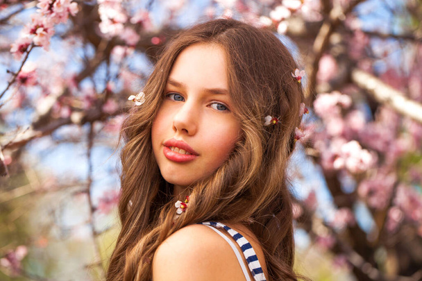 Beauty teen girl posing near blossom cherry tree with pink flowers. Spring park - 写真・画像