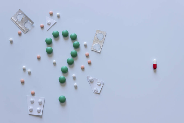 Tabletten in Form eines Fragezeichens stehen einer roten Kapsel gegenüber. Konzeptfindung und Schaffung eines Heilmittels für eine Infektionskrankheit. - Foto, Bild