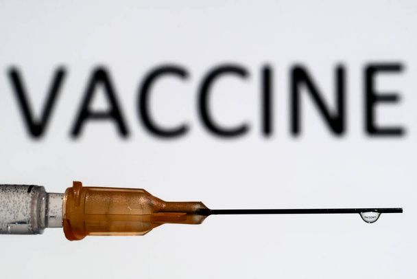 A medical needle with a droplet suspended refracting the word Vaccine, which is also out of focus in the background. - Foto, immagini