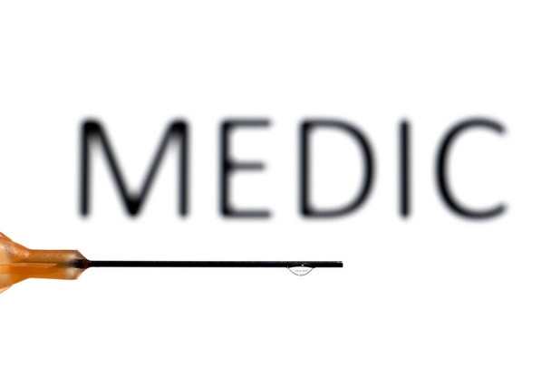 A medical needle with a droplet suspended refracting the word medic, which is also out of focus in the background - Photo, Image