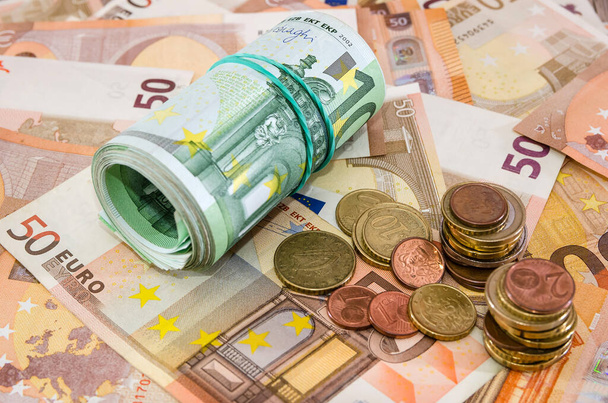 concetto di business. Primo piano arrotolato in un rotolo di 100 euro e monete su uno sfondo di banconote in euro
. - Foto, immagini