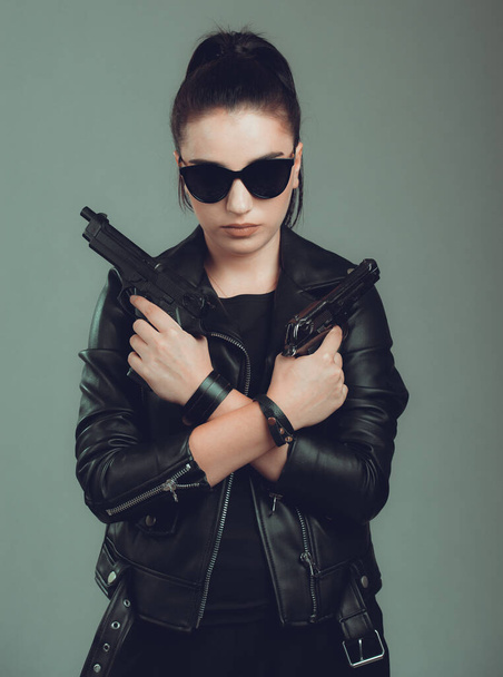 Shot of a sexy military woman posing with guns,in a black jacket,black glasses in the eyes, - Фото, изображение
