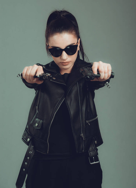 Shot of a sexy military woman posing with guns,in a black jacket,black glasses in the eyes - Foto, Bild